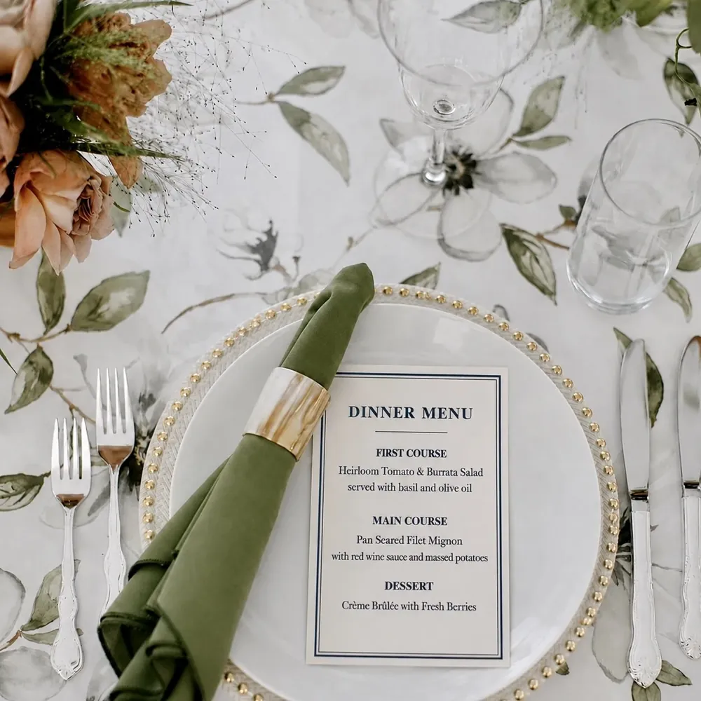 A dinner menu on a plate with a sage napkin and floral linens